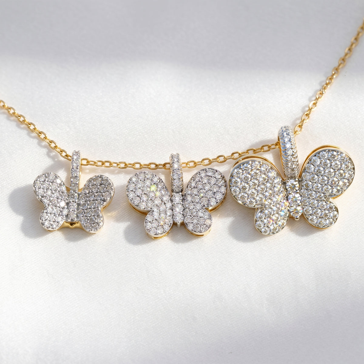 18K two-tone gold and diamond butterfly charm pendants in three sizes, shown together on one chain, small at left
