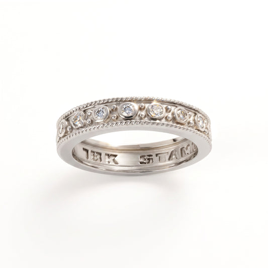 Bezel set diamond stackable band ring in 18K white gold, angled view showing the inside stamp