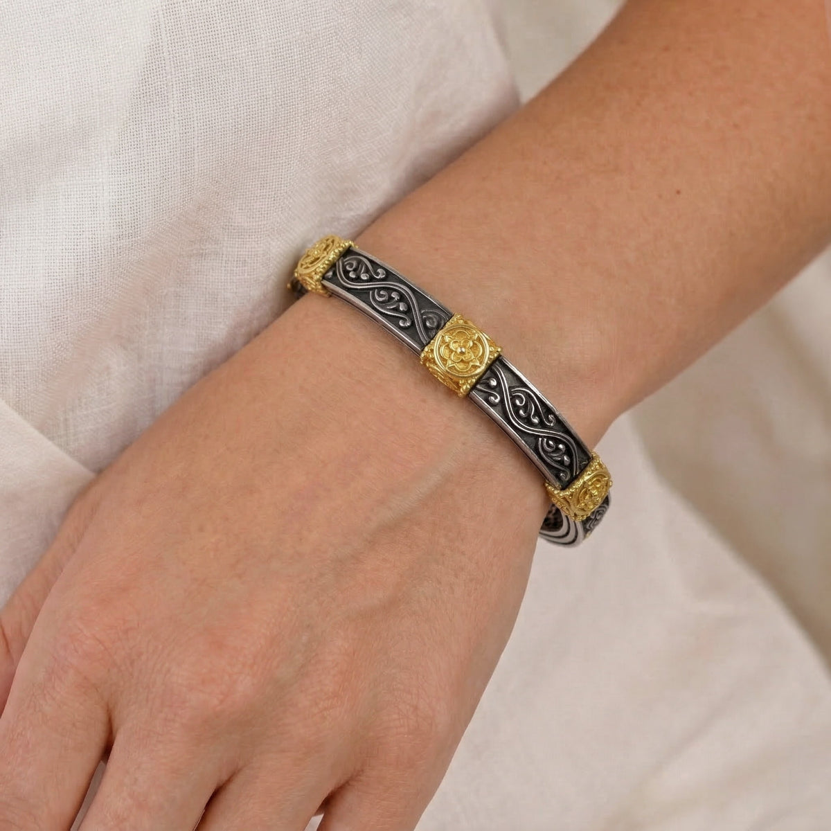 "Beginnings" bangle bracelet in aged silver and 18K gold with scrollwork, worn on the wrist