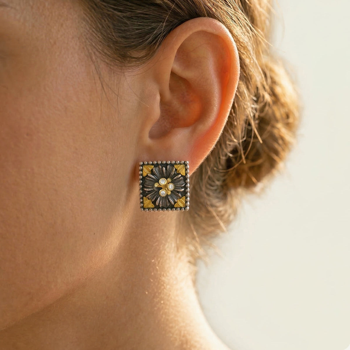 "Organza" diamond floral stud earring in aged silver and 18K gold, worn on the ear